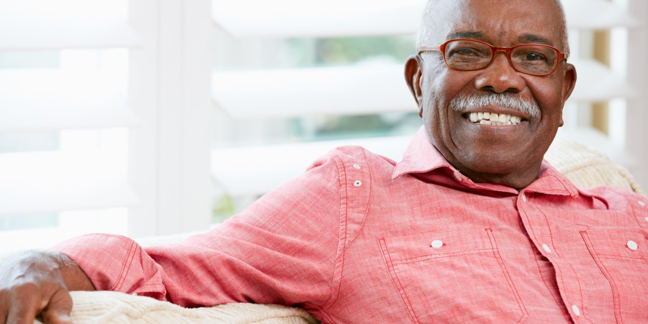 Older man with glasses smiling and sitting on couch