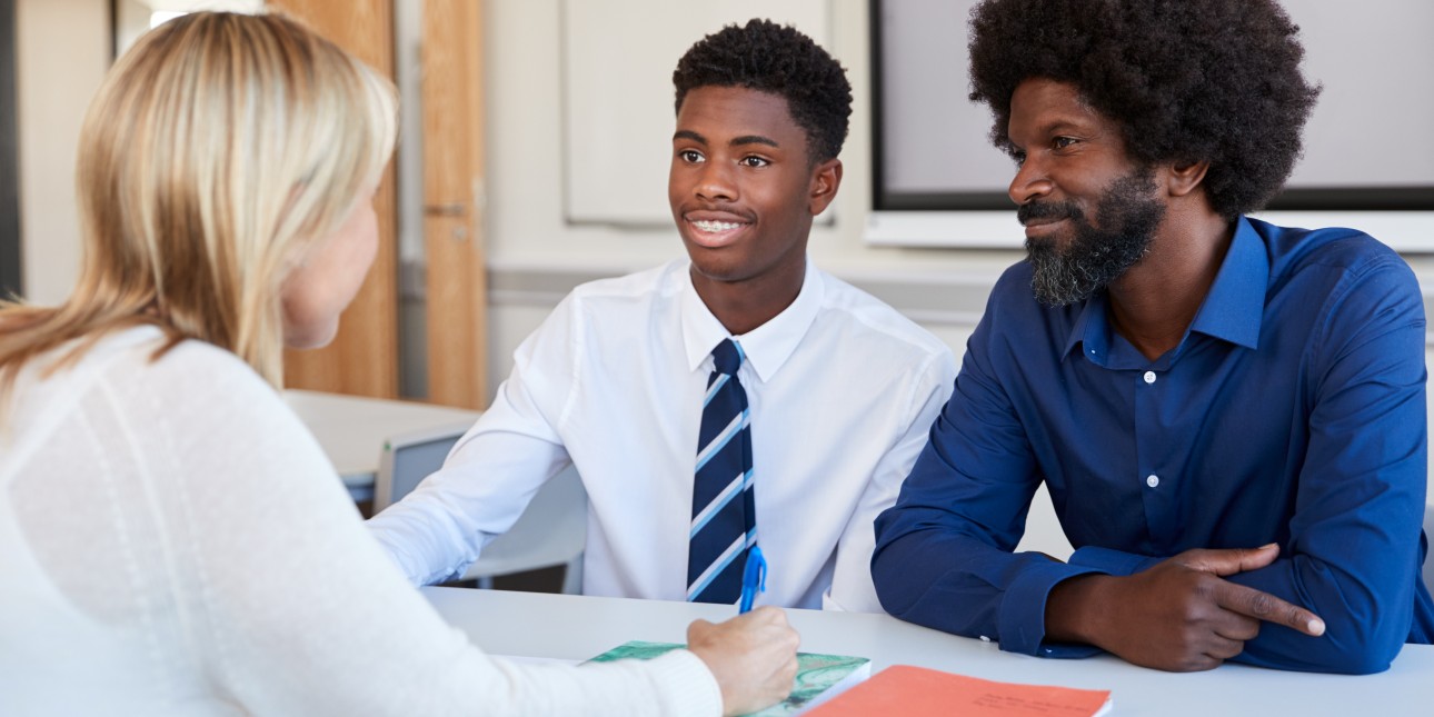 Father and son smiling in a meeting with son's teacher in active discussion.