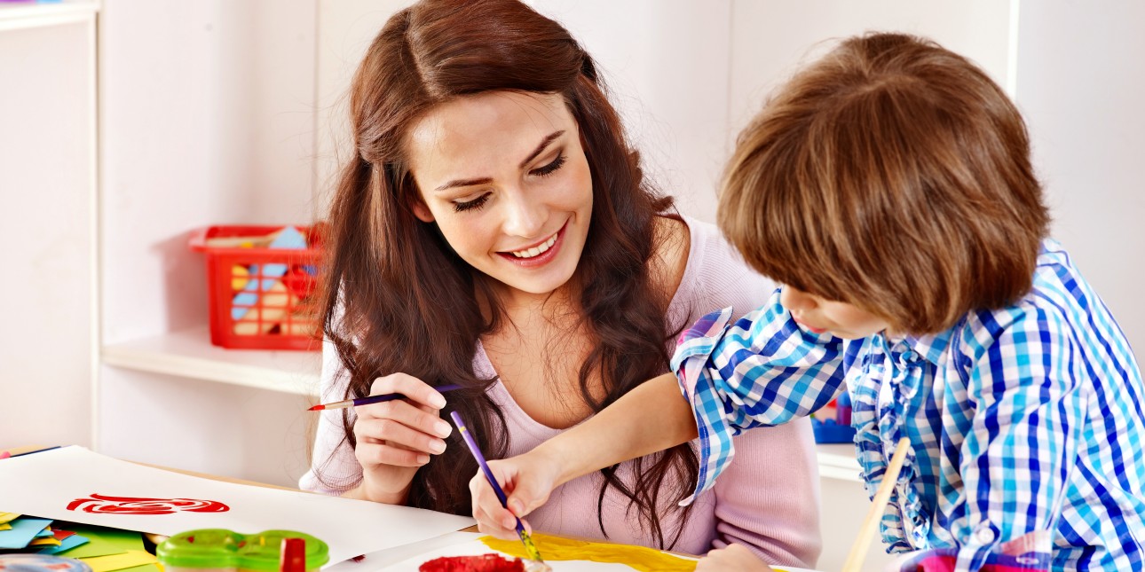 Mother and son painting at a table, mother is smiling and son is actively painting a picture.