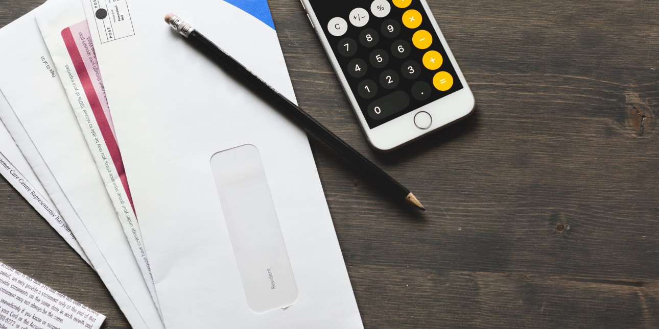 A table with a pile of envelopes, a pencil, and a cell phone with a calculator app